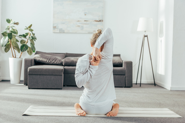 Achteraanzicht van de mens het beoefenen van yoga met handen achter rug thuis - Foto, afbeelding