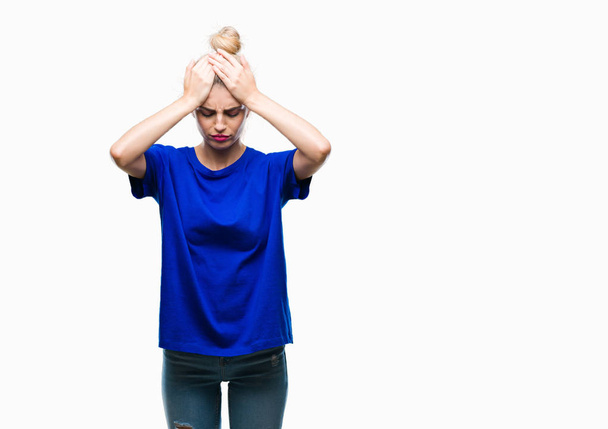 Молода красива блондинка і блакитні очі жінка в синій футболці над ізольованим тлом страждає від головного болю відчайдушно і стресу, тому що біль і мігрень. Руки на голові
. - Фото, зображення
