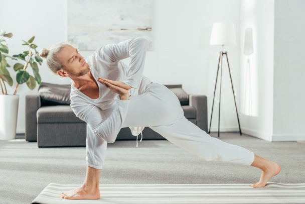 Мужчина, стоящий в вращающейся боковой уголок упражнения, Parivrtta Parsvakonasana позы на коврик для йоги дома
 - Фото, изображение