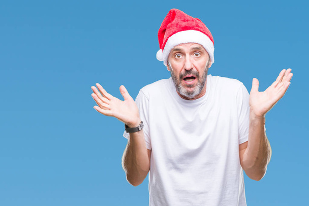 Μέση ηλικία γηραιός ανώτερος άνθρωπος φορώντας καπέλο Χριστουγέννων πάνω από απομονωμένες φόντο ανίδεοι και συγκεχυμένη έκφραση με τα χέρια που έθεσε. Έννοια της αμφιβολίας. - Φωτογραφία, εικόνα