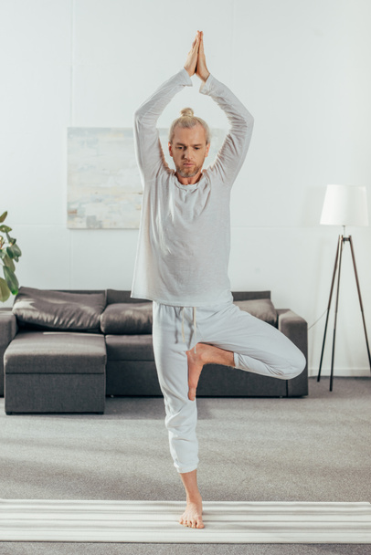 sportieve volwassen man boom pose op yoga mat thuis oefenen - Foto, afbeelding