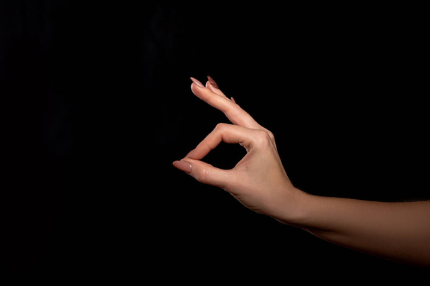 Prise de vue studio de la main d'une femme non identifiée montrant un geste de doigts que tout va bien ou OK sur un fond noir
 - Photo, image