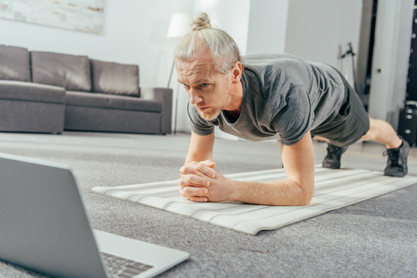 sporty adult man doing plank exercise and looking at laptop - Foto, immagini