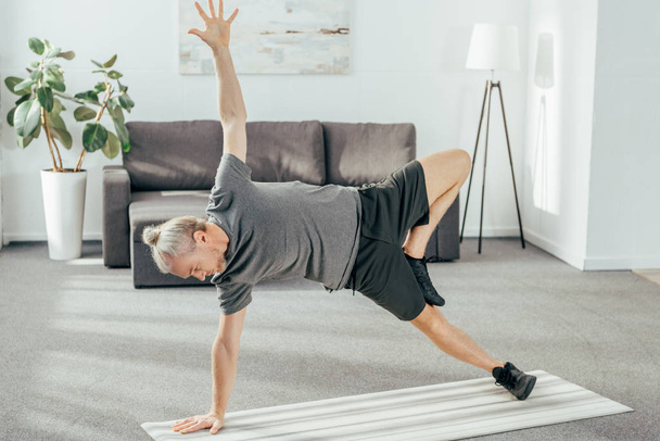 Blick aus der Vogelperspektive auf einen athletischen Mann in Sportbekleidung, der zu Hause auf einer Yogamatte praktiziert  - Foto, Bild