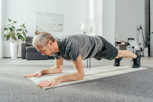 sporty adult man in sportswear doing plank exercise on yoga mat at home - 写真・画像
