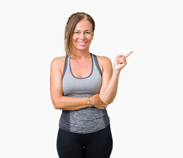 Beautiful middle age woman wearing sport clothes over isolated background with a big smile on face, pointing with hand and finger to the side looking at the camera. - Photo, Image
