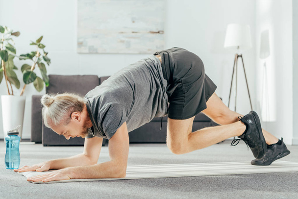 Seitenansicht des athletischen Mannes im Sportbekleidungstraining auf der Yogamatte zu Hause - Foto, Bild