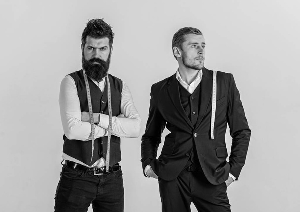 Oldfashioned against modern concept. Man with beard in waistcoat and young tailor in classic suit. Tailors on strict faces with measuring tapes around neck ready to take measurements, light background - Fotografie, Obrázek