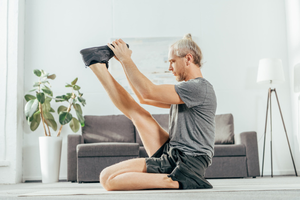 вид сбоку спортивного взрослого мужчины, растягивающегося на коврике для йоги дома
 - Фото, изображение