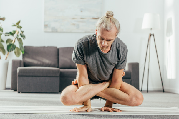 homem adulto praticando ioga em casa e fazendo exercício de equilíbrio de braço com pernas cruzadas, postura em escala, Tolasana, Utpluthi Pose
 - Foto, Imagem
