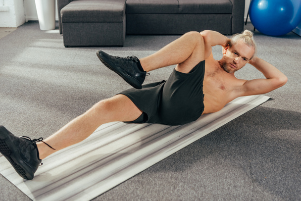 gespierde shirtless man doen abs oefening op yoga mat thuis - Foto, afbeelding