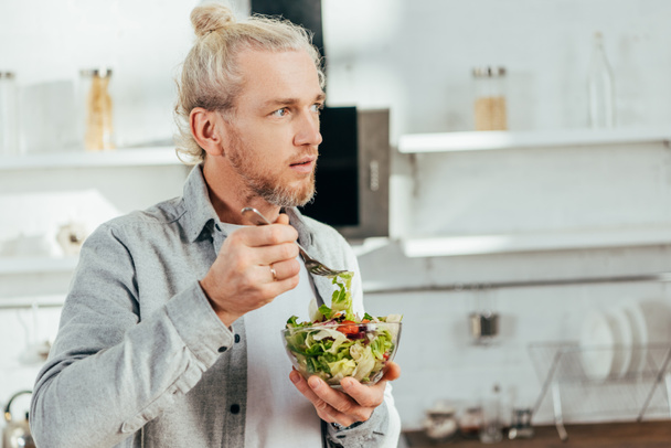 sebze salatası yemek ve uzak mutfakta seyir yakışıklı adam - Fotoğraf, Görsel