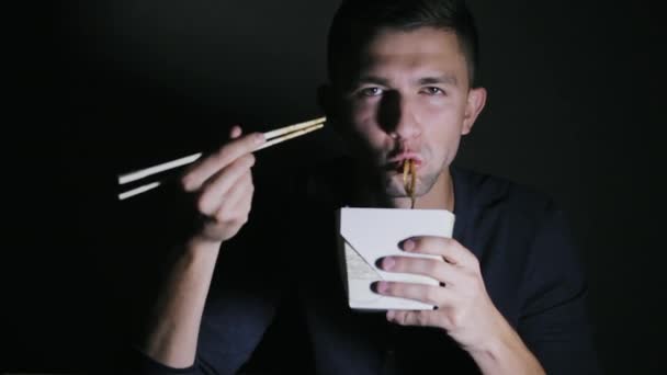 Close-up of a man who is eating noodles with chopsticks from a box. European eating Chinese food - Imágenes, Vídeo