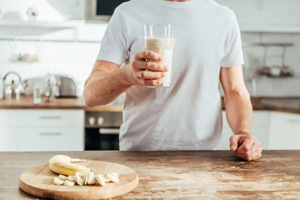 cropped shot of athletic man holding glass with banana protein shake at home - 写真・画像