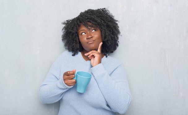 Молода жінка над сірий гранж стіни пити чашечку кави серйозним обличчям, думаючи про питання, дуже плутати ідея - Фото, зображення