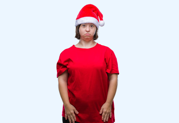 Молодая взрослая женщина с синдромом Дауна носит рождественскую шляпу на изолированном фоне с серьезным выражением лица. Простой и естественный взгляд на камеру
. - Фото, изображение