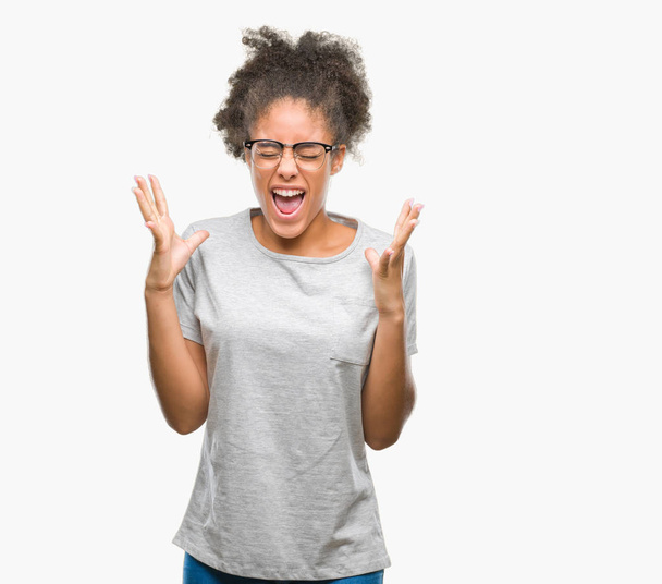 Giovane donna afro-americana con gli occhiali su sfondo isolato che celebra pazzo e pazzo per il successo con le braccia alzate e gli occhi chiusi urlando eccitato. Concetto vincitore
 - Foto, immagini