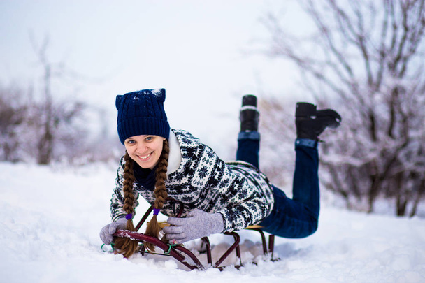Εύθυμη νεαρή γυναίκα Έχοντας διασκέδαση σε έλκηθρο στο χιονισμένο καιρικές συνθήκες - Φωτογραφία, εικόνα