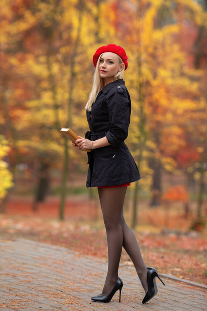 Beautiful blonde girl with perfect legs and red beret posing outdoor on the street of autumn park. Modern Little Red Riding Hood in the forest. - Foto, imagen