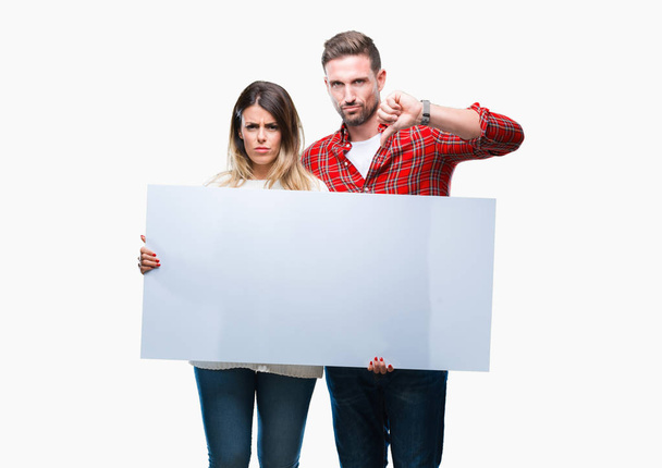 Молодая пара вместе держит пустой баннер на изолированном фоне с сердитым лицом, негативный знак, показывающий неприязнь с опущенными пальцами, концепция отказа
 - Фото, изображение