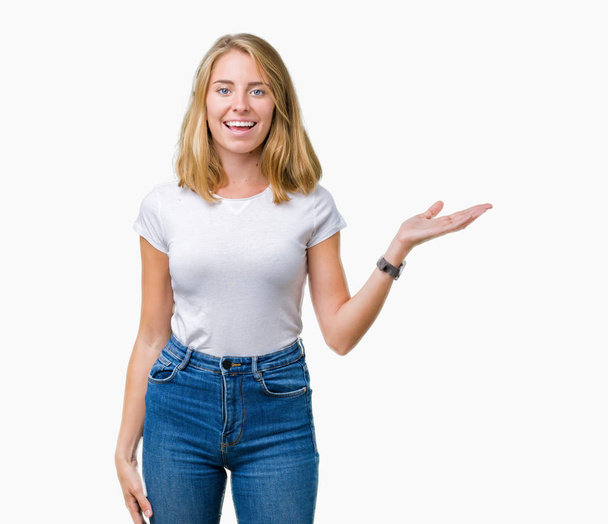 Beautiful young woman wearing casual white t-shirt over isolated background smiling cheerful presenting and pointing with palm of hand looking at the camera. - Photo, Image
