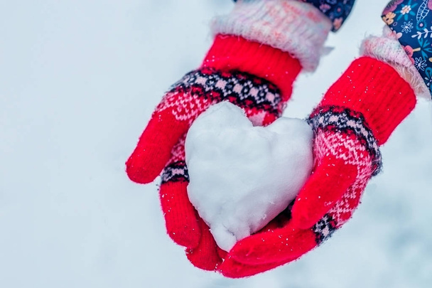 Herz aus Schnee in den Händen des Mädchens. Hände in Strickhandschuhen mit rotem Herz aus Schnee. - Foto, Bild