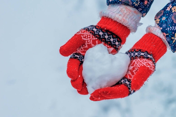 Herz aus Schnee in den Händen des Mädchens. Hände in Strickhandschuhen mit rotem Herz aus Schnee. - Foto, Bild