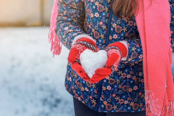 Girl in red knitted mittens holding a heart of snow. - Fotografie, Obrázek