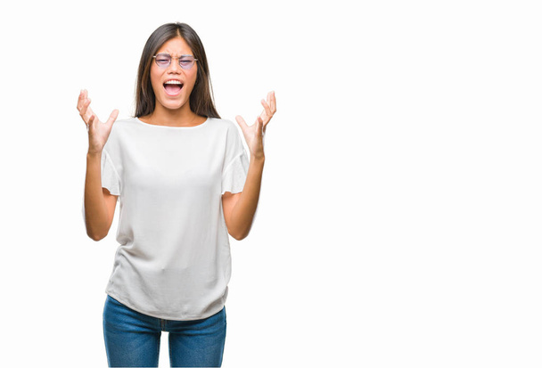 Young asian woman wearing glasses over isolated background crazy and mad shouting and yelling with aggressive expression and arms raised. Frustration concept. - Foto, imagen