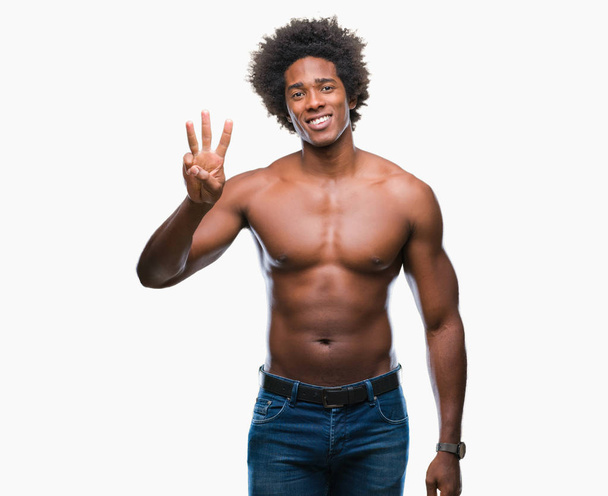 Afro americano sin camisa hombre mostrando desnudo cuerpo sobre aislado fondo mostrando y señalando hacia arriba con los dedos número tres mientras sonríe confiado y feliz
. - Foto, imagen