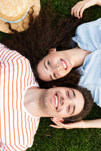 Image from top of beautiful couple man and woman 20s lying alongside opposite heads on green grass in park - Foto, imagen