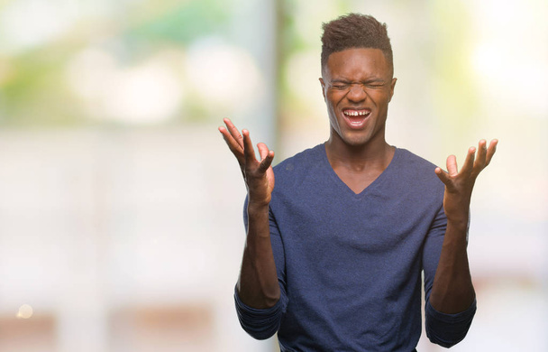 junger afrikanisch-amerikanischer Mann mit isoliertem Hintergrund feiert verrückt und erfolgsverrückt mit erhobenen Armen und geschlossenen Augen, die aufgeregt schreien. Siegerkonzept - Foto, Bild