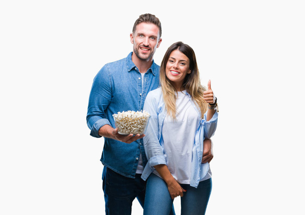 Jeune couple amoureux manger du pop-corn sur fond isolé heureux avec un grand sourire faisant signe ok, pouce levé avec les doigts, excellent signe
 - Photo, image