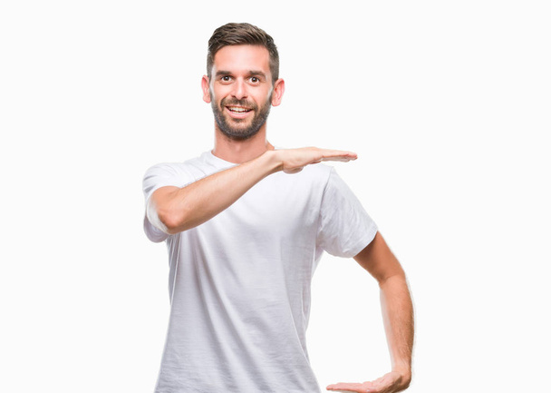Jonge knappe man over geïsoleerde achtergrond gebaren met de handen tonen grote en grote grootte teken, symbool van de maatregel. Glimlachend kijken naar de camera. Meten concept. - Foto, afbeelding