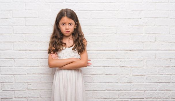 Young hispanic kid over white brick wall skeptic and nervous, disapproving expression on face with crossed arms. Negative person. - Foto, imagen