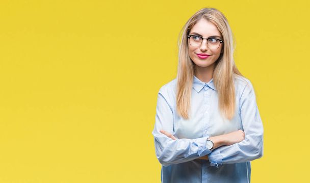 Молодая красивая блондинка бизнес-женщина в очках на изолированном фоне улыбается, глядя в сторону и думая
. - Фото, изображение