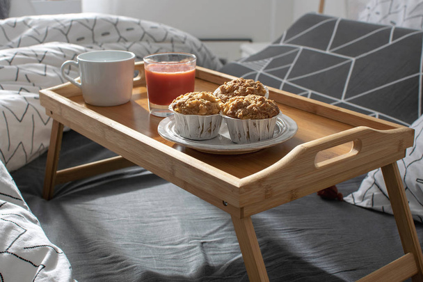 Christmas morning, Valentines day, cozy morning, hotel room - breakfast in bed, wooden tray with coffee, muffins, apple, orange juice on the bed. Modern scandinavian bedroom interior. - Фото, изображение
