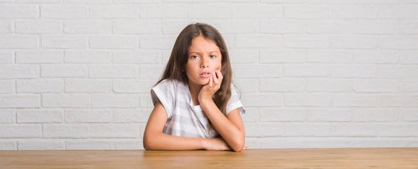 Criança hispânica jovem sentada na mesa em casa tocando a boca com a mão com expressão dolorosa por causa da dor de dente ou doença dentária nos dentes. Conceito de dentista
. - Foto, Imagem