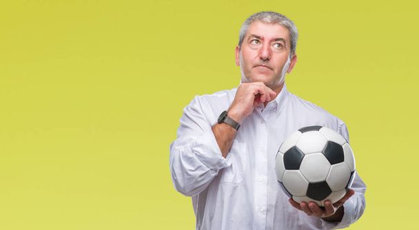 Bell'uomo anziano che tiene palla da calcio su sfondo isolato faccia seria pensando alla domanda, idea molto confusa
 - Foto, immagini