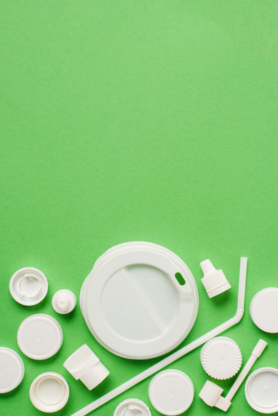Bovenaanzicht van wegwerp plastic doppen, stro en deksel voor drankje drinken op groene achtergrond - Foto, afbeelding