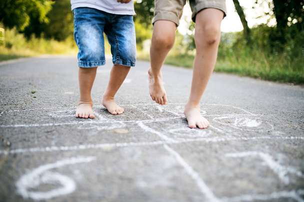 Two small boys hopscotching on a road in park on a summer day. - Foto, imagen