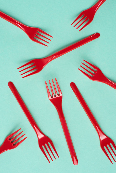 Top view of red plastic forks scattered on blue background - Foto, afbeelding