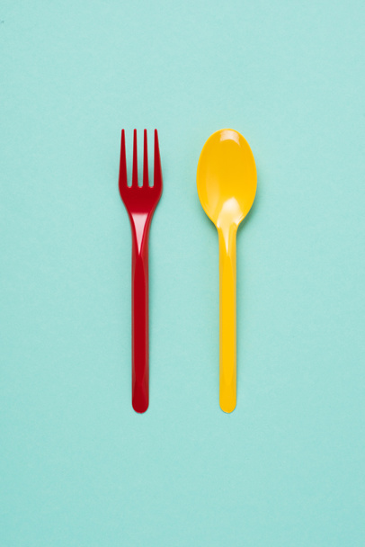 Top view of red plastic fork and yellow spoon on blue background - Фото, зображення