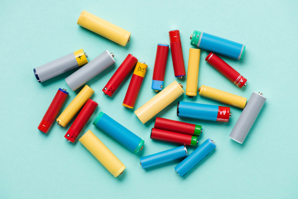 Bovenaanzicht van kleurrijke batterijen verspreid op blauwe achtergrond - Foto, afbeelding