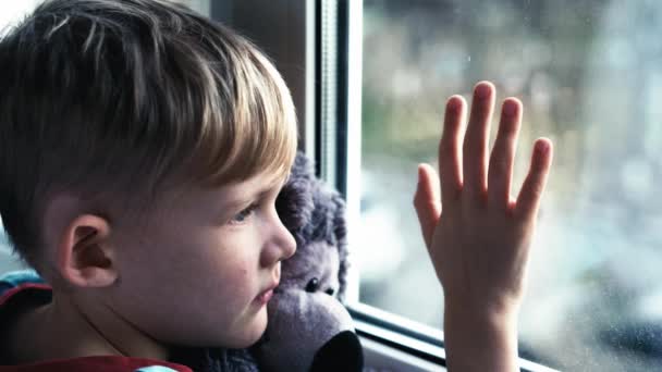 Smutny chłopiec samotny dzieckiem z niedźwiedzia w pobliżu patrząc przez okno. Mały chłopiec dziecko jest w depresji. - Materiał filmowy, wideo