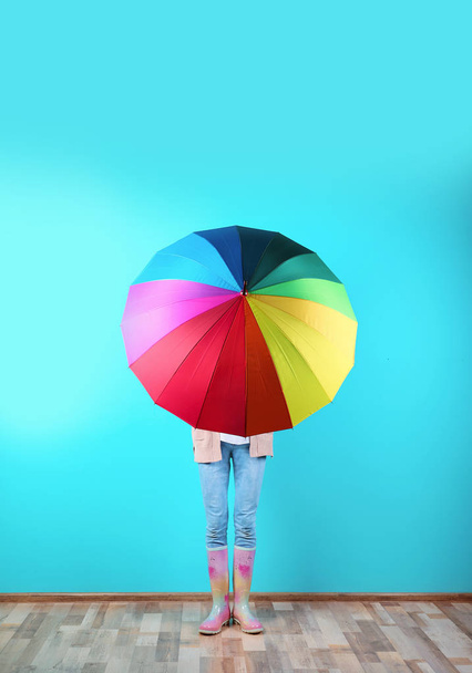 Woman hiding behind rainbow umbrella near color wall - Foto, imagen