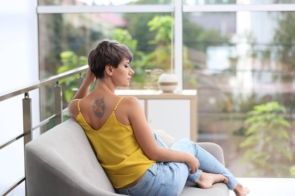 Trendy young woman with tattoo on sofa indoors - Foto, immagini