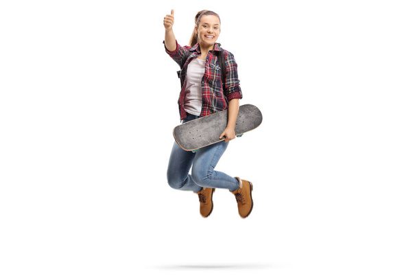 Volledige lengte portret van een vreugdevolle tienermeisje met een rugzak en een skateboard maken een duim omhoog gebaar geïsoleerd op witte achtergrond - Foto, afbeelding