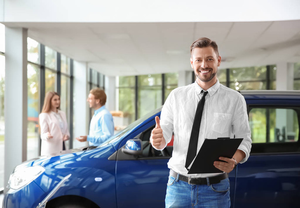 Salesman with clipboard near new car in modern auto dealership - Photo, image
