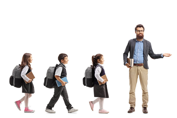 Full length profile shot of schoolchildren walking in a line and a teacher gesturing welcome with his hand and looking into the camera isolated on white background - Foto, immagini